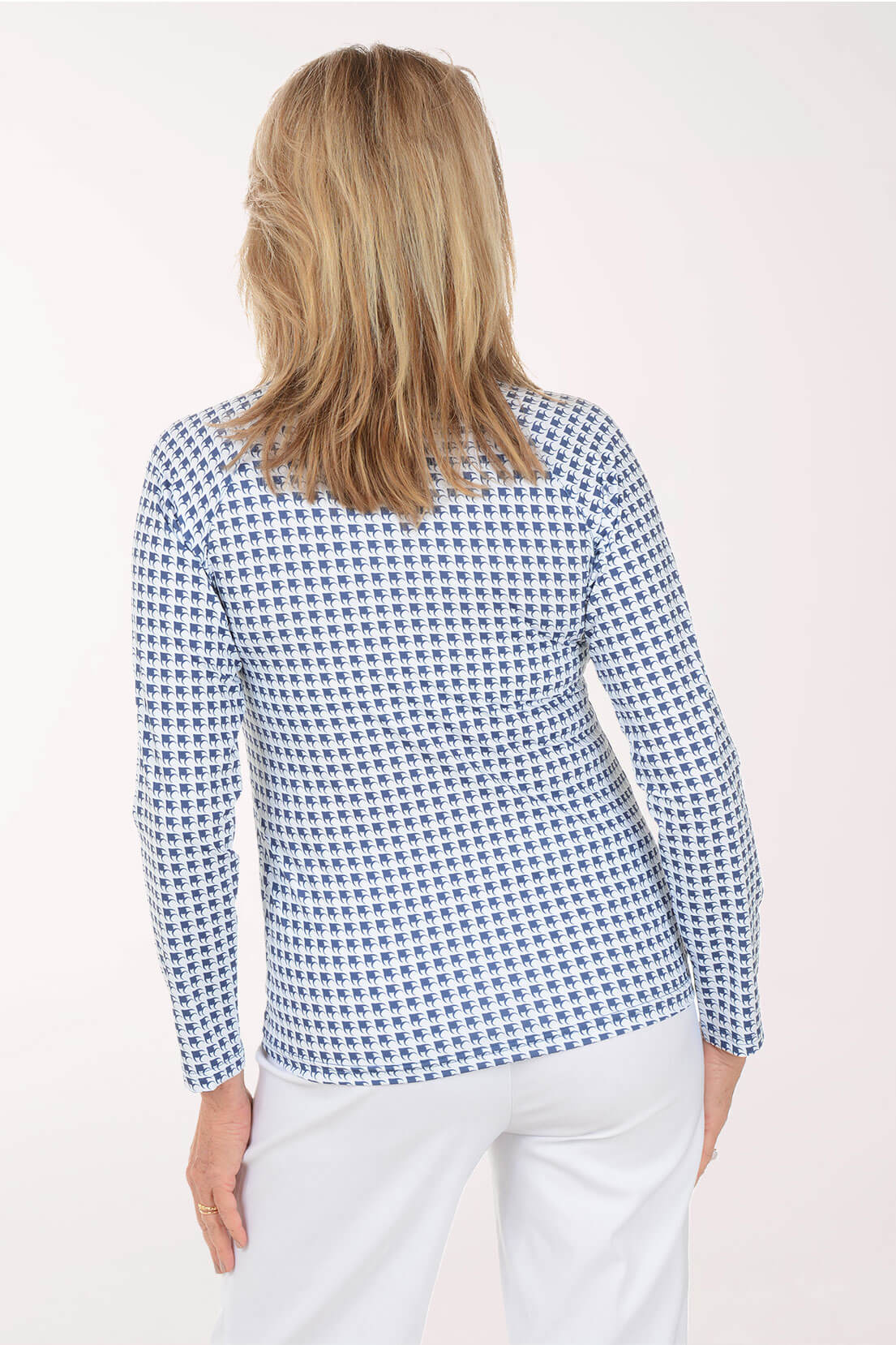 A woman viewed from the back wearing a long-sleeve top with a small blue and white geometric pattern, paired with white pants, against a plain light background.