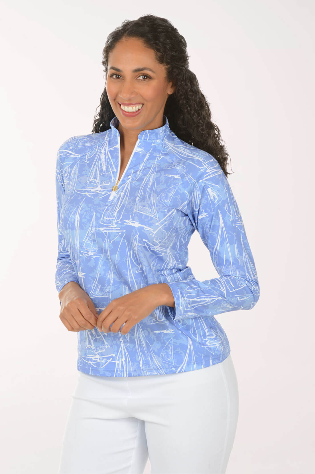 A woman modeling a light blue long-sleeve golf shirt with a white abstract pattern and a half-zip collar, paired with white pants, against a plain white studio background.