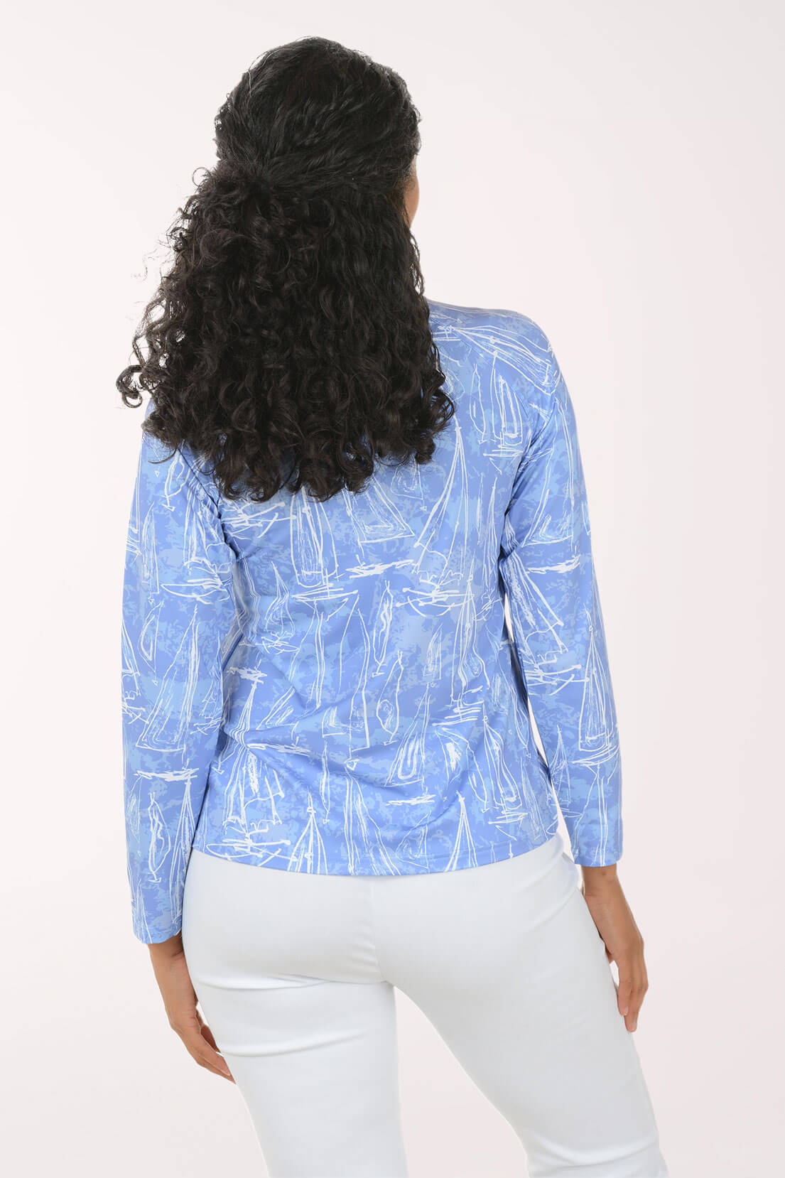 A woman viewed from behind wearing a light blue long-sleeve top with a white abstract line pattern and white pants, against a plain light background.