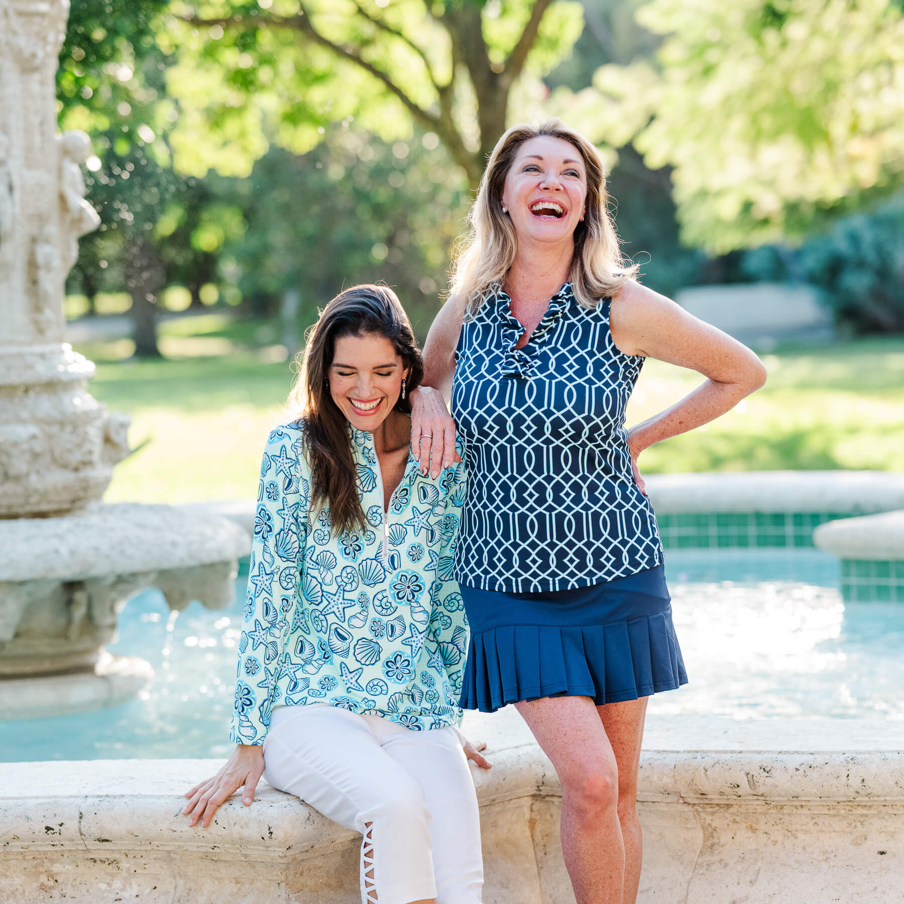 Two women posing together in a park with a fountain in the background