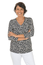 Woman wearing a black and white giraffe patterned blouse with white pants on a white background.