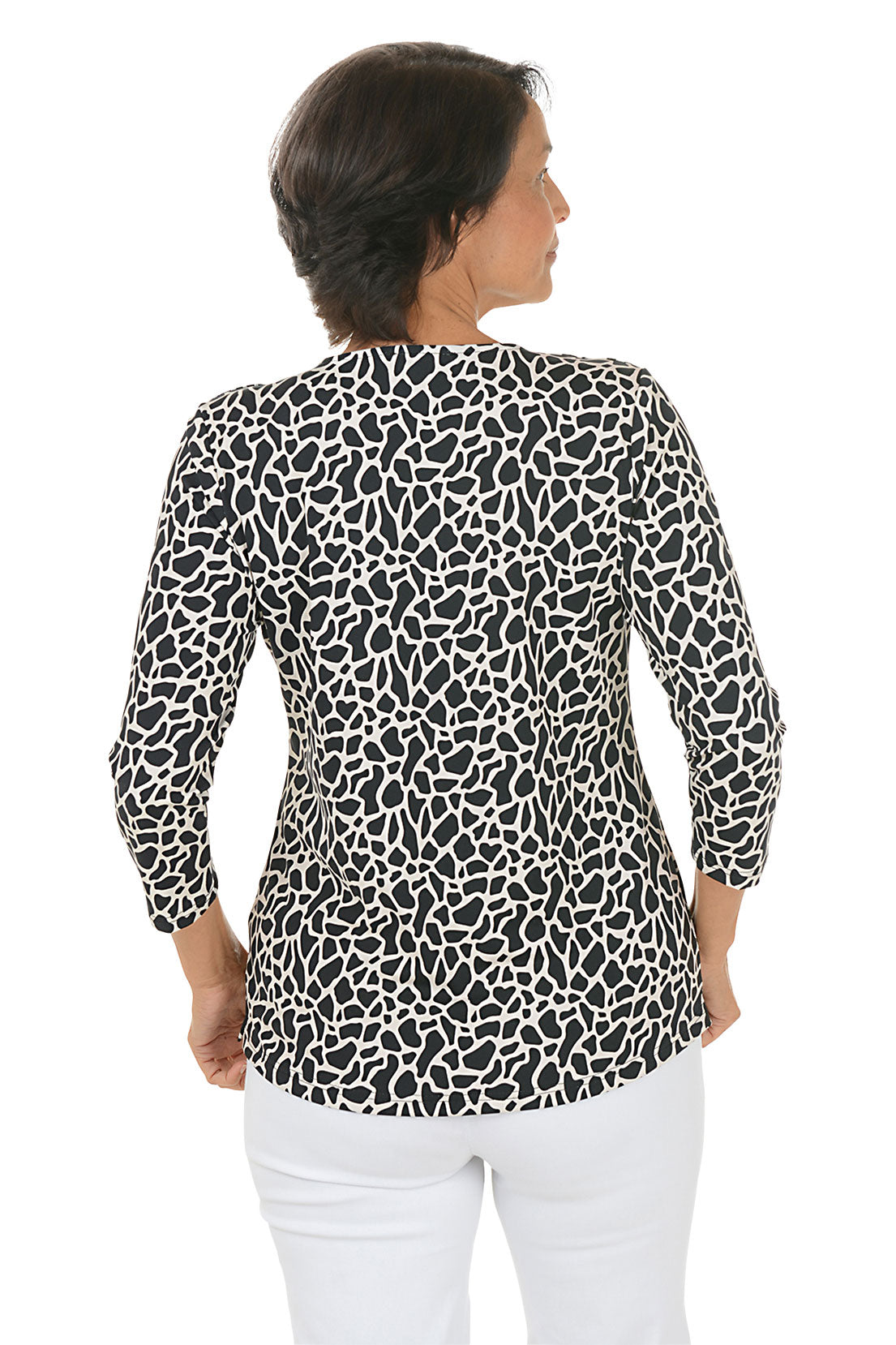 Woman wearing a black and white giraffe patterned blouse with white pants on a white background. Back shot.
