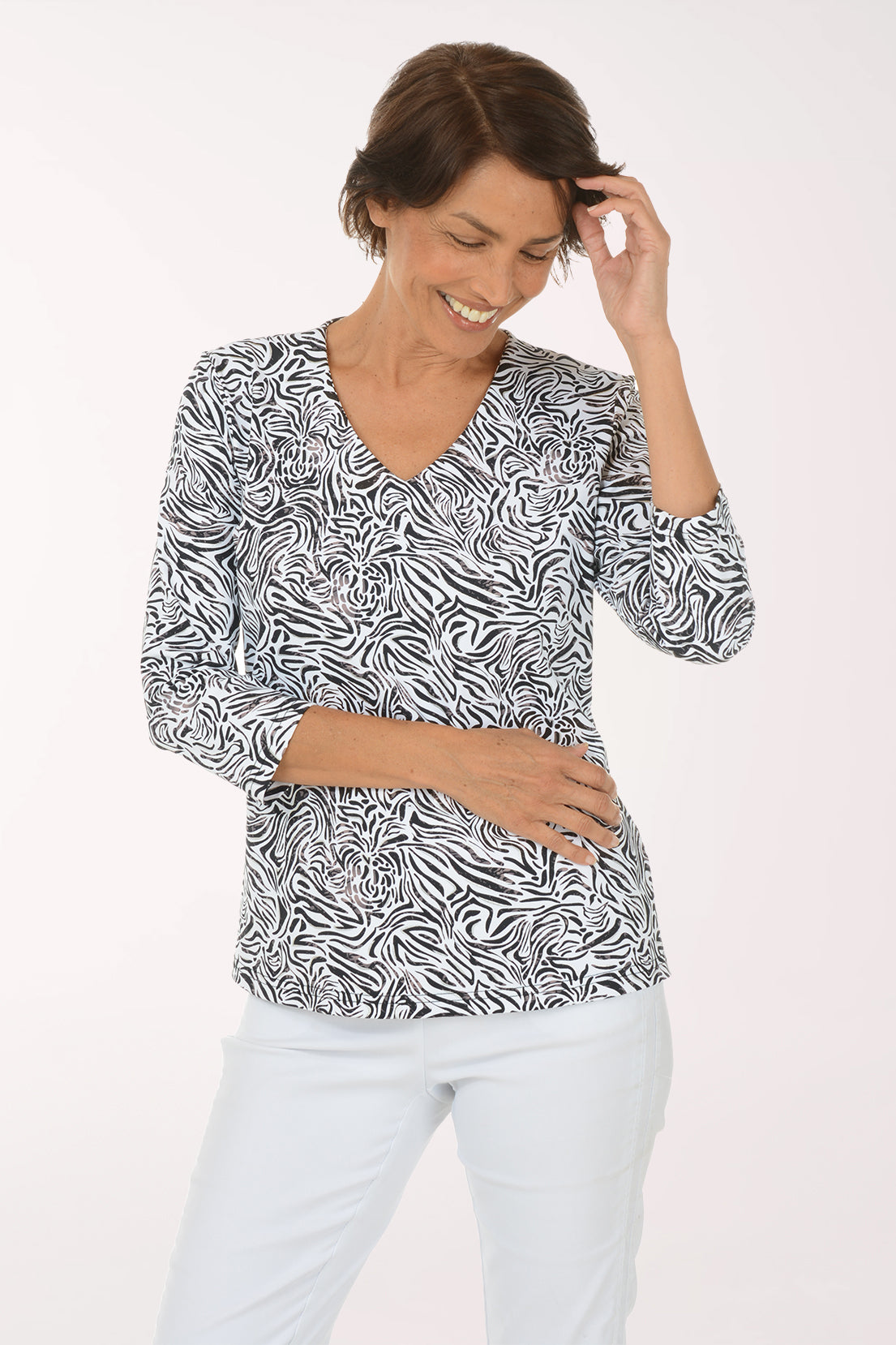 A woman touching her hair and smiling down in the Silver Zebra Swirl UPF50+ V-Neck Top, showing the V-neckline and silver foil accents in the zebra print.