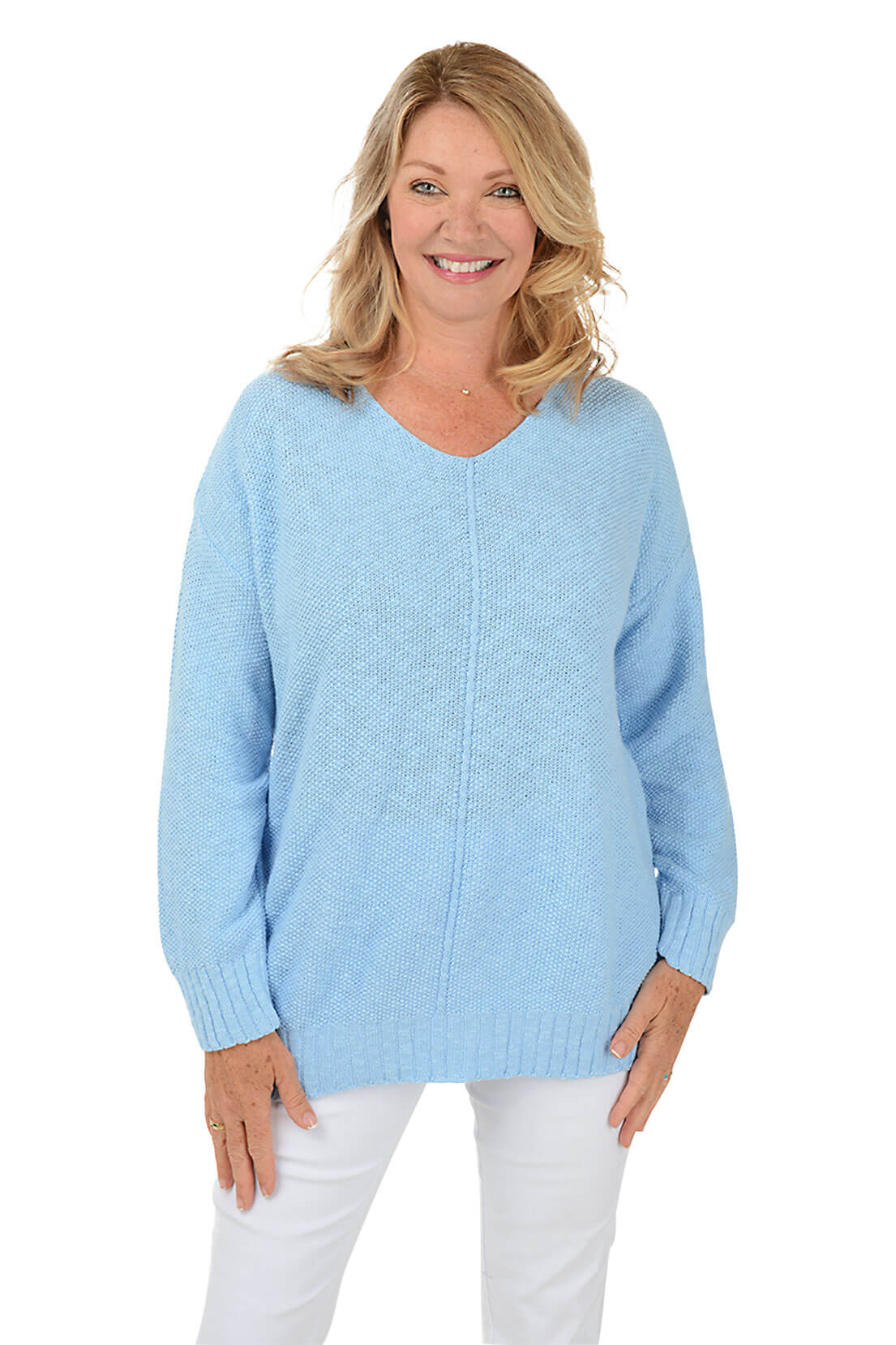 A woman wearing a long sleeve sky blue cotton V-neck sweater, with a seam down the front and white pants.