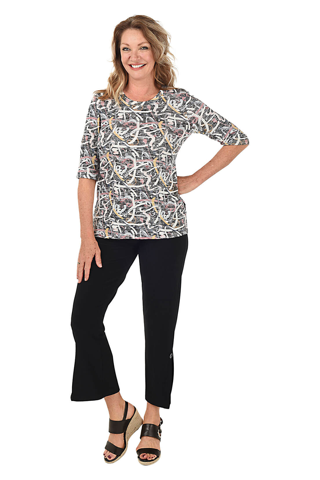 A model wearing black ankle pants with a split hemline featuring a decorative button, paired with a white top and black sandals. Full length shot.