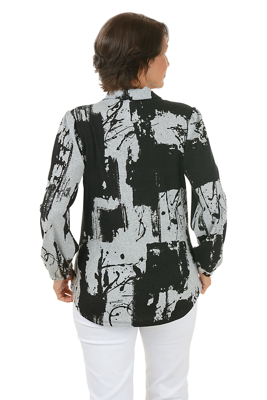 Woman wearing a black and white abstract patterned blouse with white pants on a white background. Back shot.