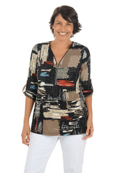 Woman wearing a colorful patterned blouse with white pants on a white background.