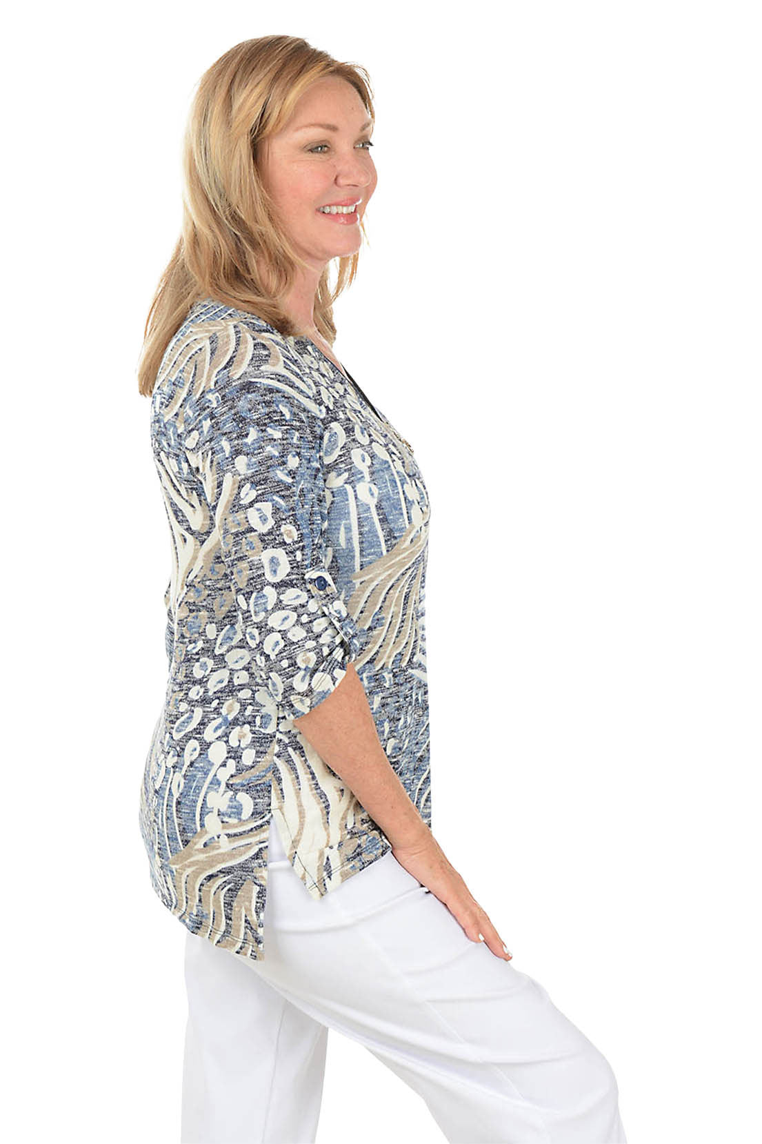 Woman wearing a patterned blouse with white pants on a white background. Side shot.