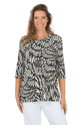 Woman wearing a black and white patterned top with white pants on a white background.
