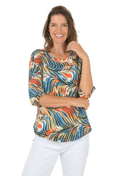 Woman wearing a colorful patterned top and white pants on a white background.