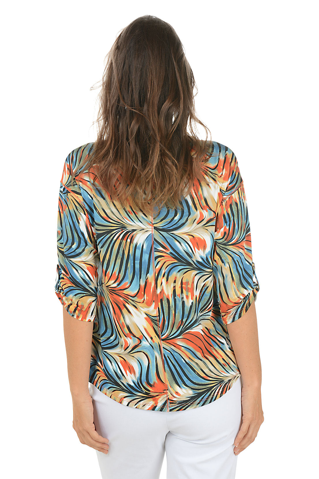 Woman wearing a colorful patterned top and white pants on a white background. Back shot.