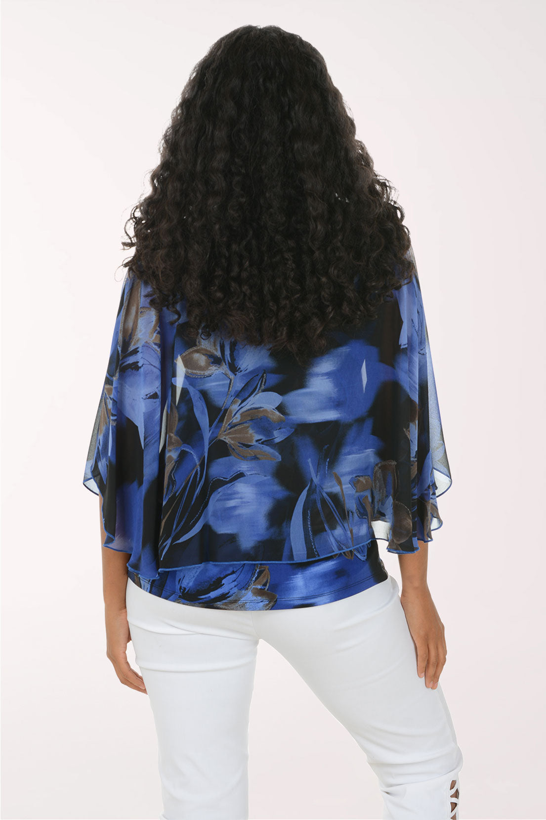 A woman wearing a blue and black abstract floral print blouse with wide flutter sleeves, paired with white pants, photographed against a plain light background.