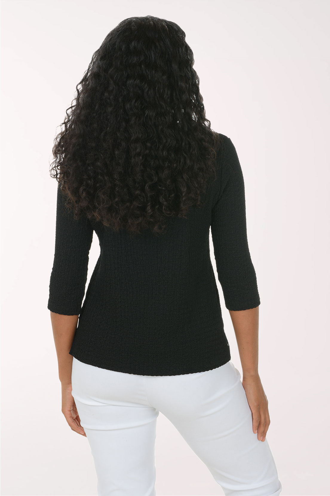 A woman shown from the back wearing a black three-quarter sleeve ribbed knit top and white pants, against a plain light background.