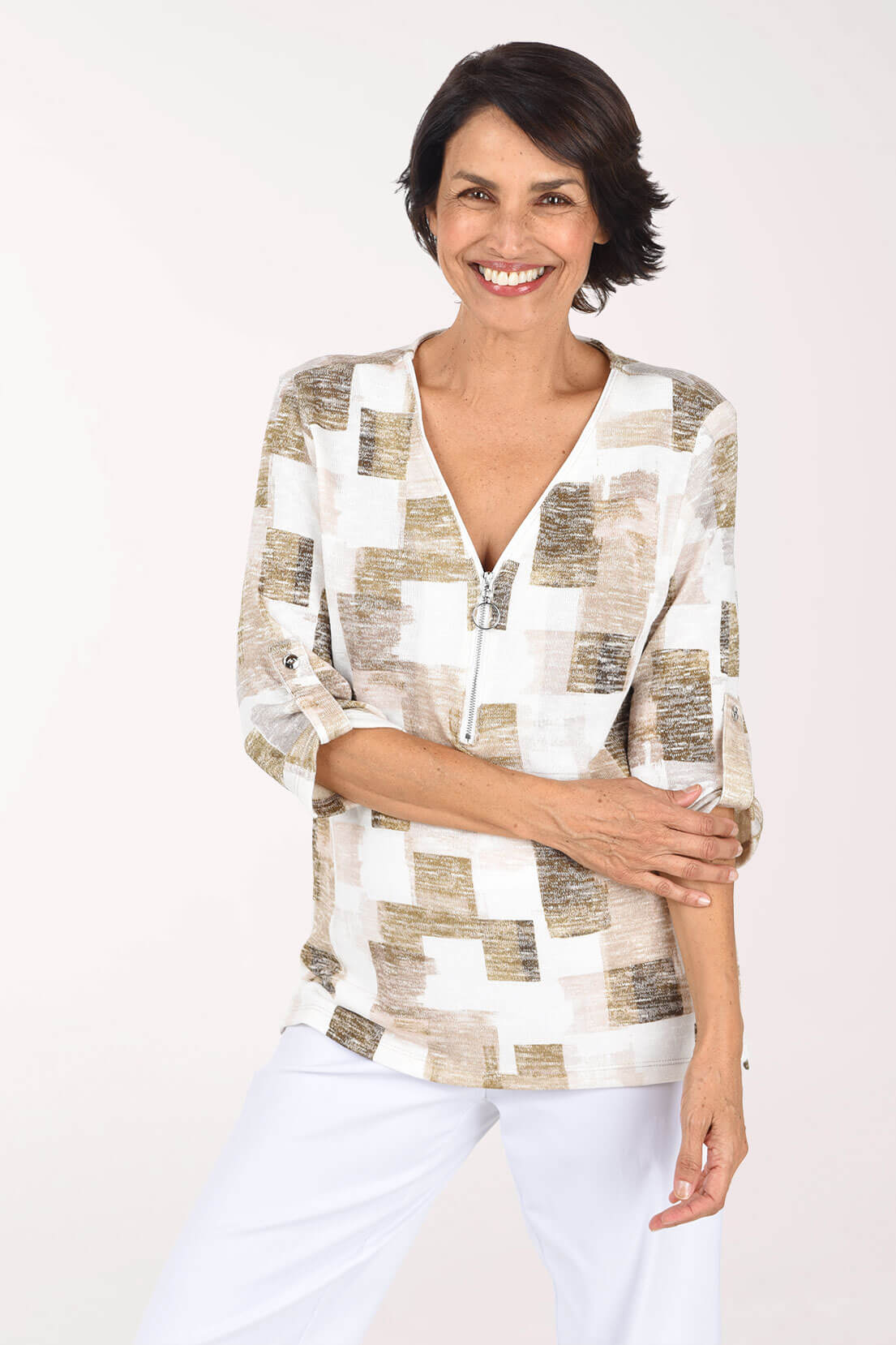 Model wearing a white, beige, and blush abstract print knit top with a zip V-neck and roll-tab sleeves, paired with white pants.