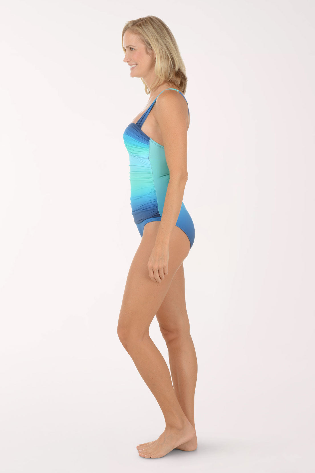 Woman wearing a blue and green gradient swimsuit on a white background. Side shot.