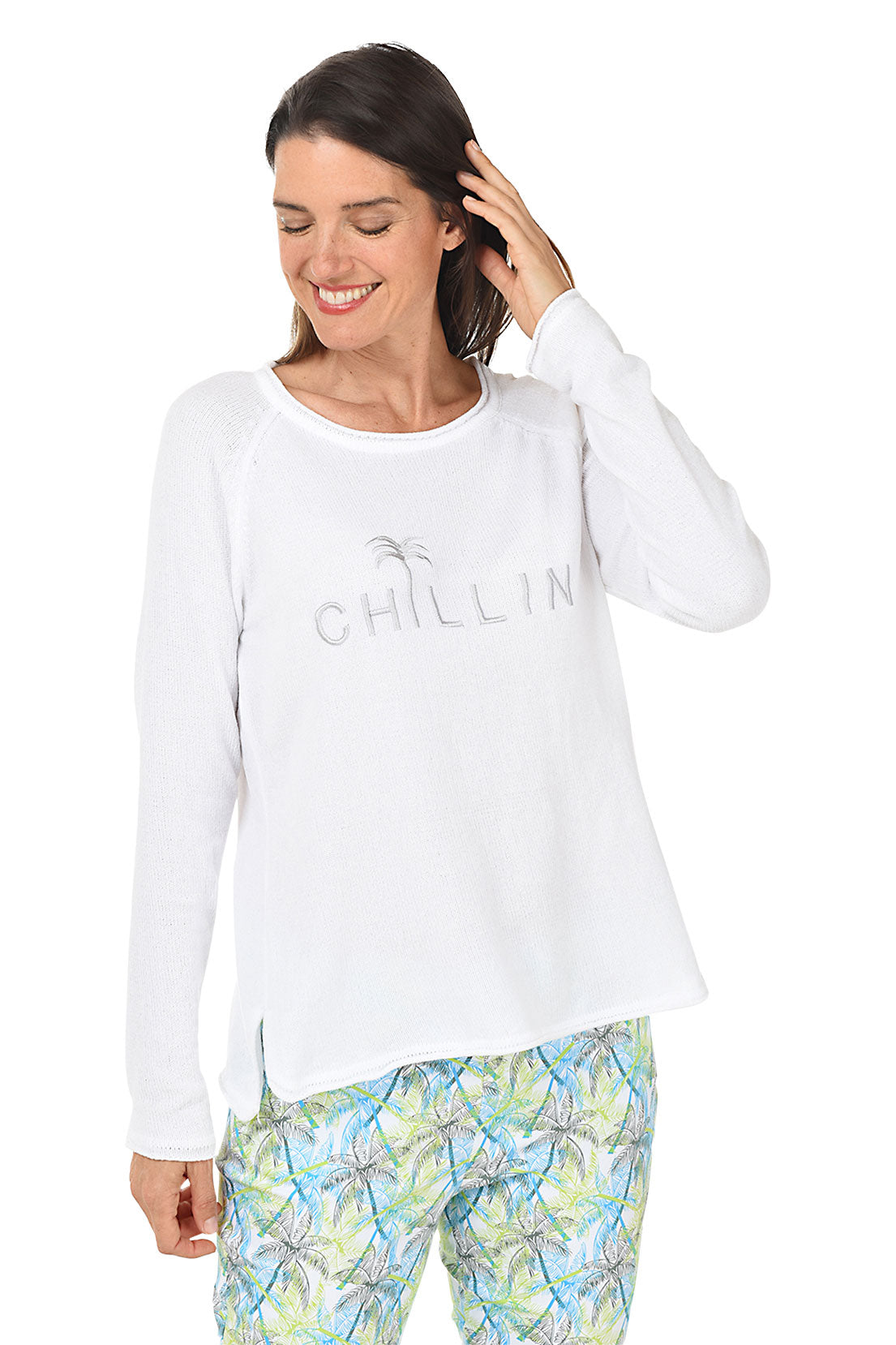 Woman wearing a white long-sleeve sweater with 'Chillin' text and colorful pants on a white background.