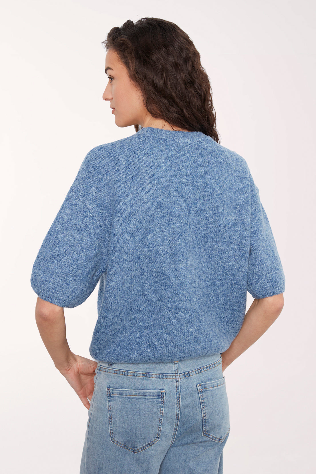 A woman shown from the back wearing a textured, heathered blue short-sleeve knit top and light blue jeans against a plain white studio background.