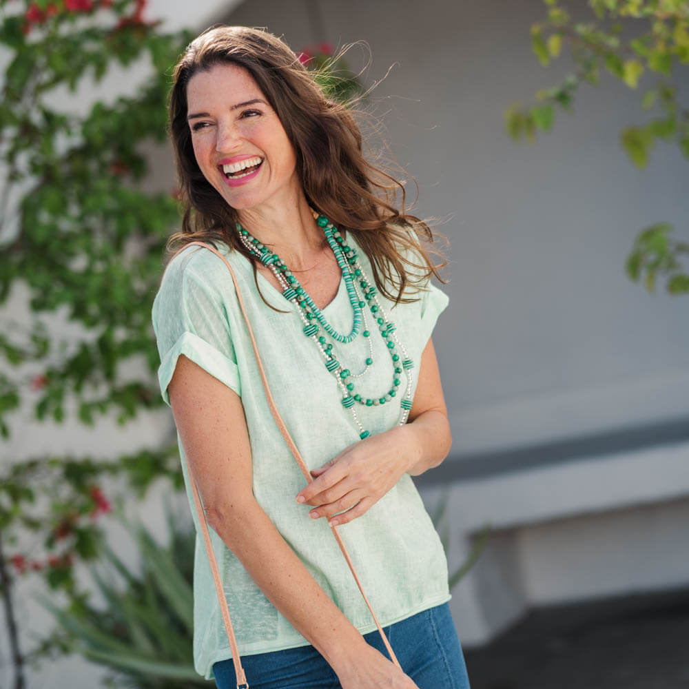 Woman wearing a light green top and blue jeans with a necklace, standing outdoors.