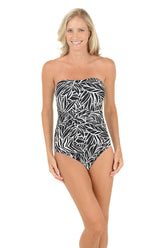 A woman wearing a black and white strapless bandeau one piece swimsuit with a single removable halter strap.