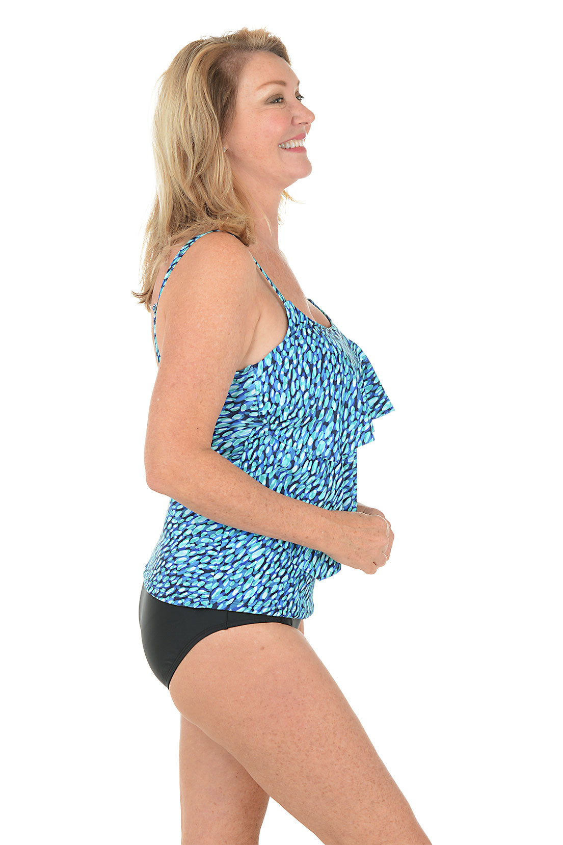 Woman wearing a blue and black patterned tankini top on a white background. Side shot.