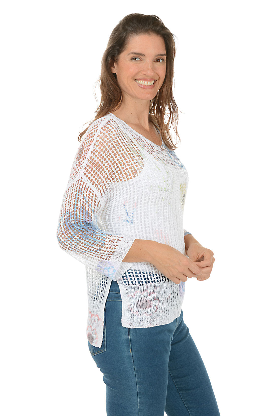 A woman wearing a floral watercolor crochet high-low sweater in white, with 3/4 dolman sleeves and a high-low hemline. Side shot.