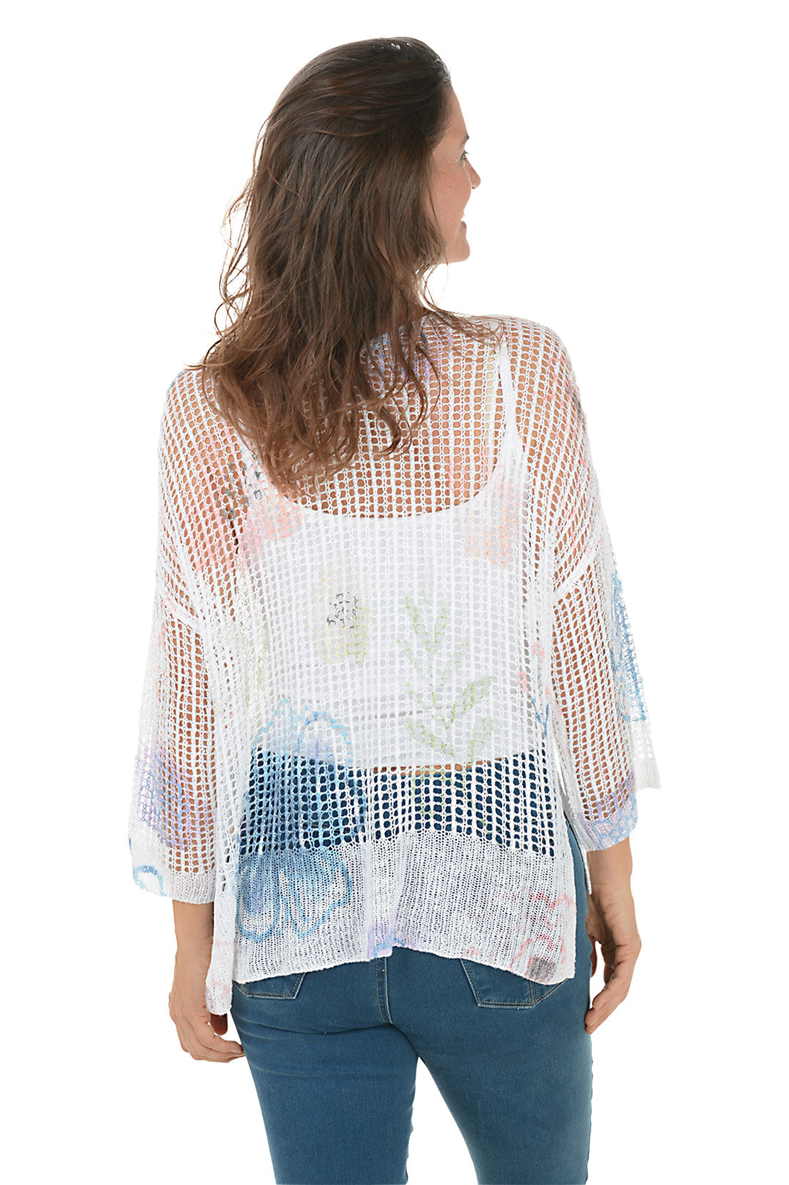 A woman wearing a floral watercolor crochet high-low sweater in white, with 3/4 dolman sleeves and a high-low hemline. Back shot.