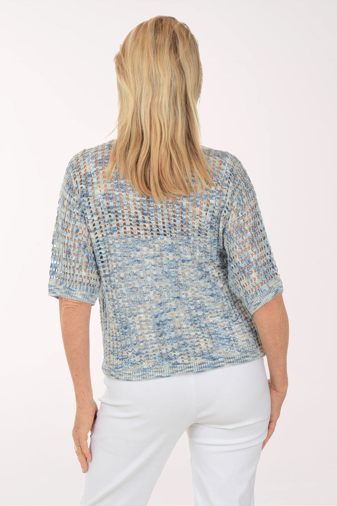Woman wearing a textured blue top and white pants on a white background