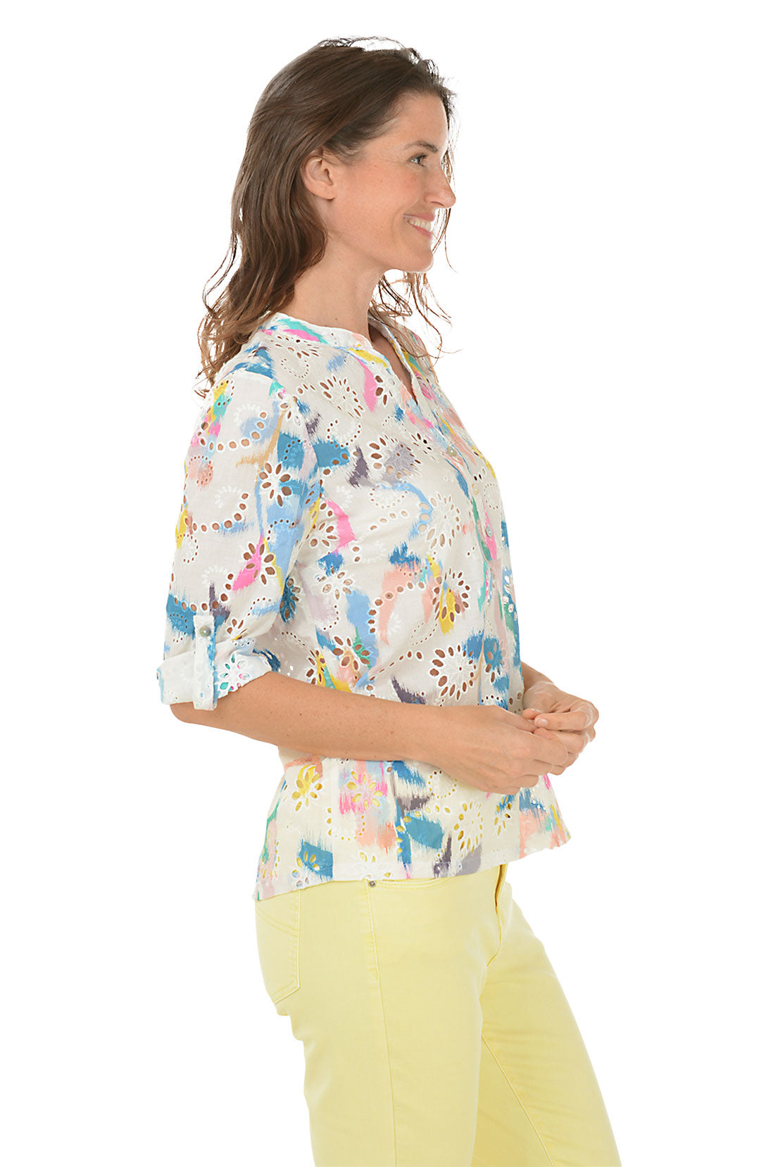 A woman wearing a multicolored floral eyelet lace cotton blouse with a mandarin collar and 3/4 sleeves, paired with yellow pants. Side shot.