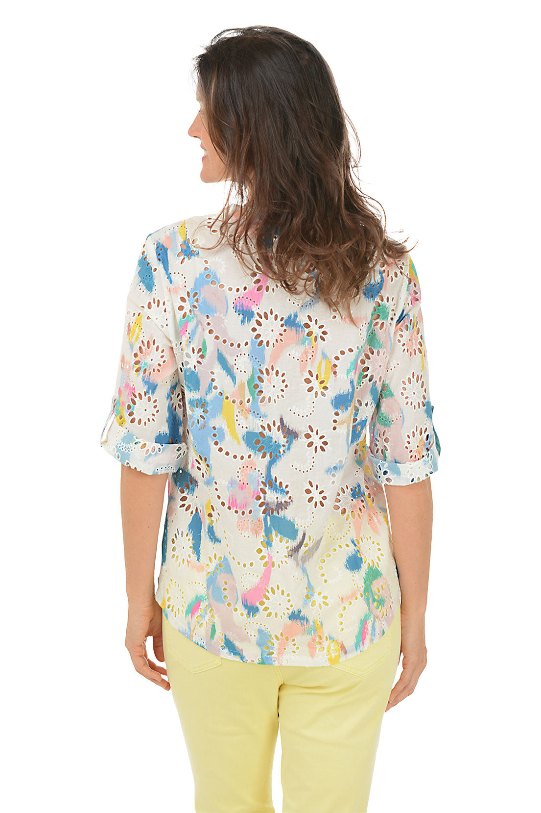A woman wearing a multicolored floral eyelet lace cotton blouse with a mandarin collar and 3/4 sleeves, paired with yellow pants. Back shot.