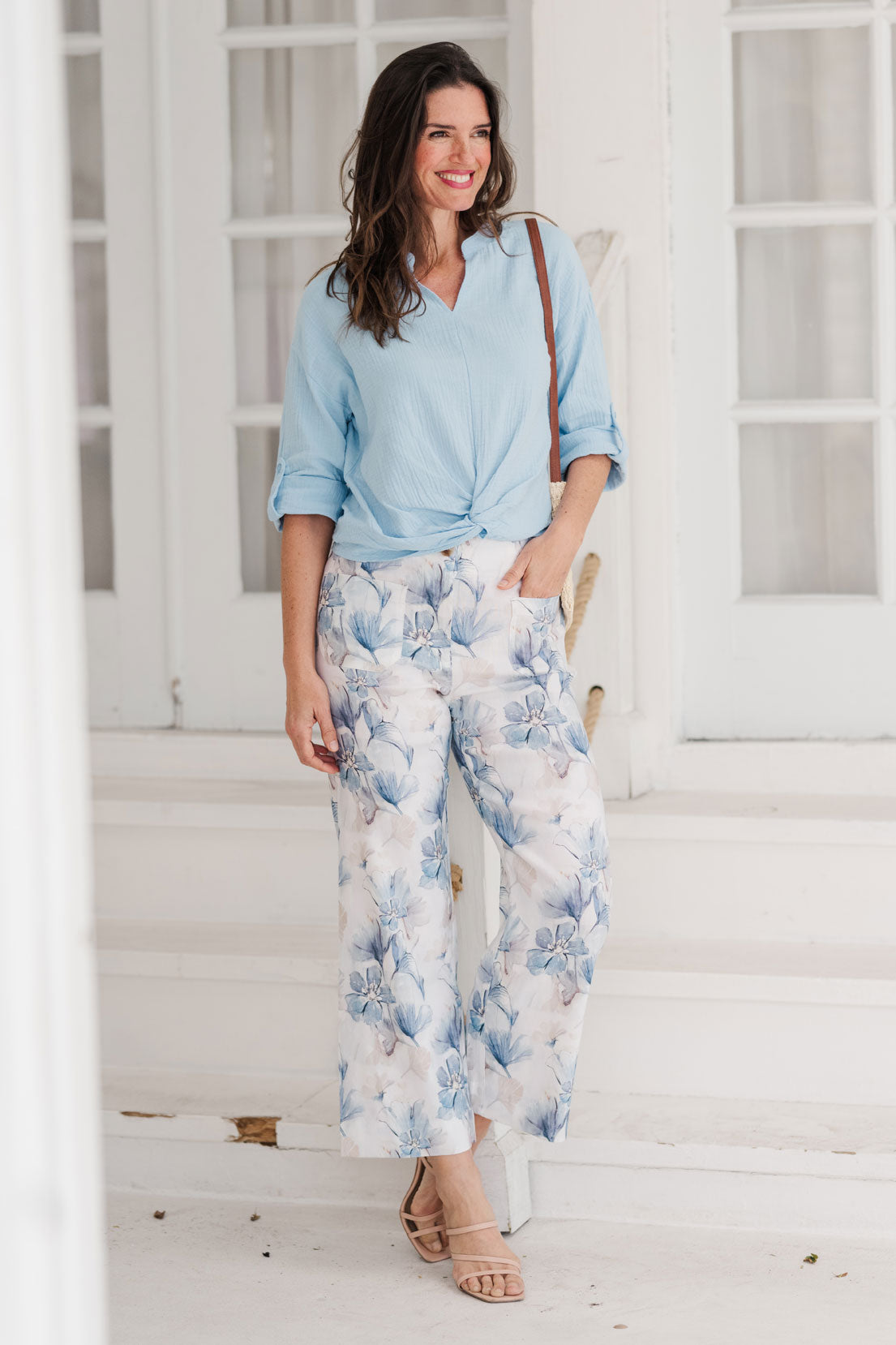 Woman wearing a light blue shirt and floral pants standing on a white staircase.