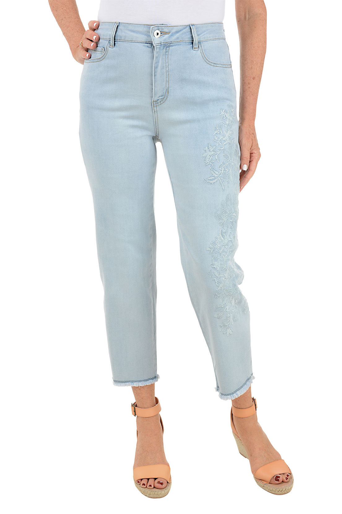 A pair of light blue denim ankle pants with embroidery on the left leg and frayed hemline, displayed on a model wearing tan sandals.