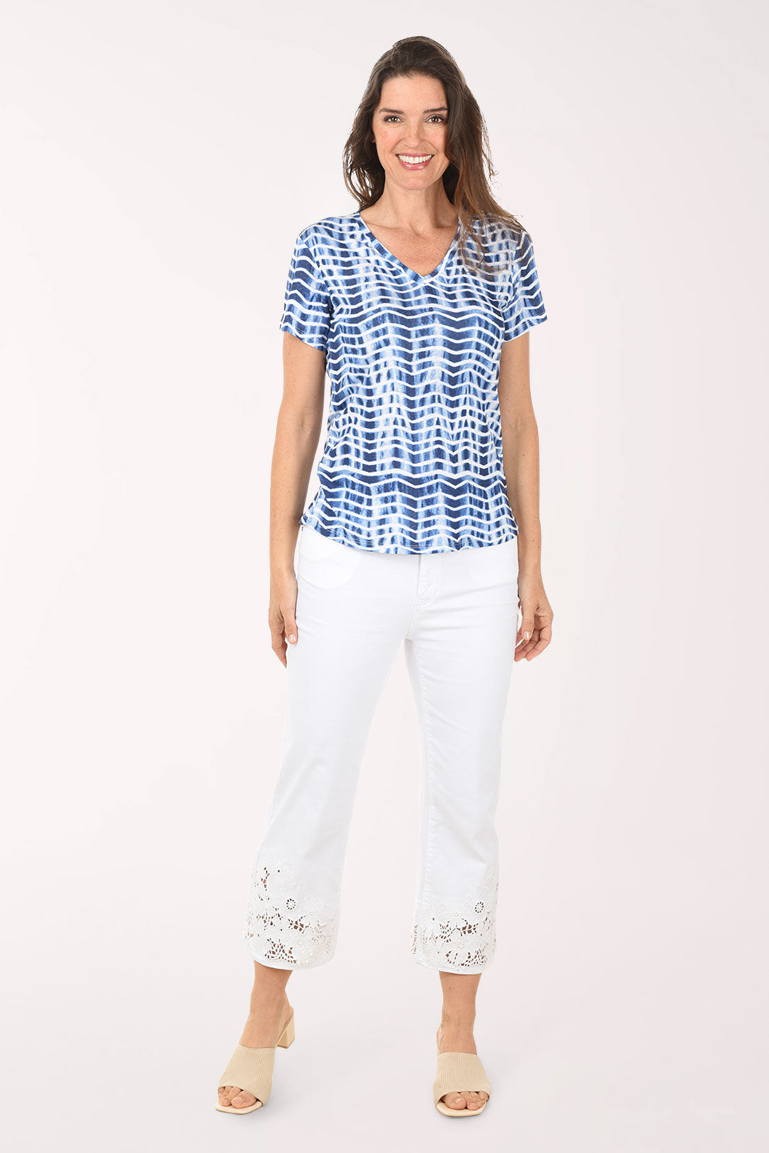 Woman wearing a blue and white patterned top with white pants on a white background
