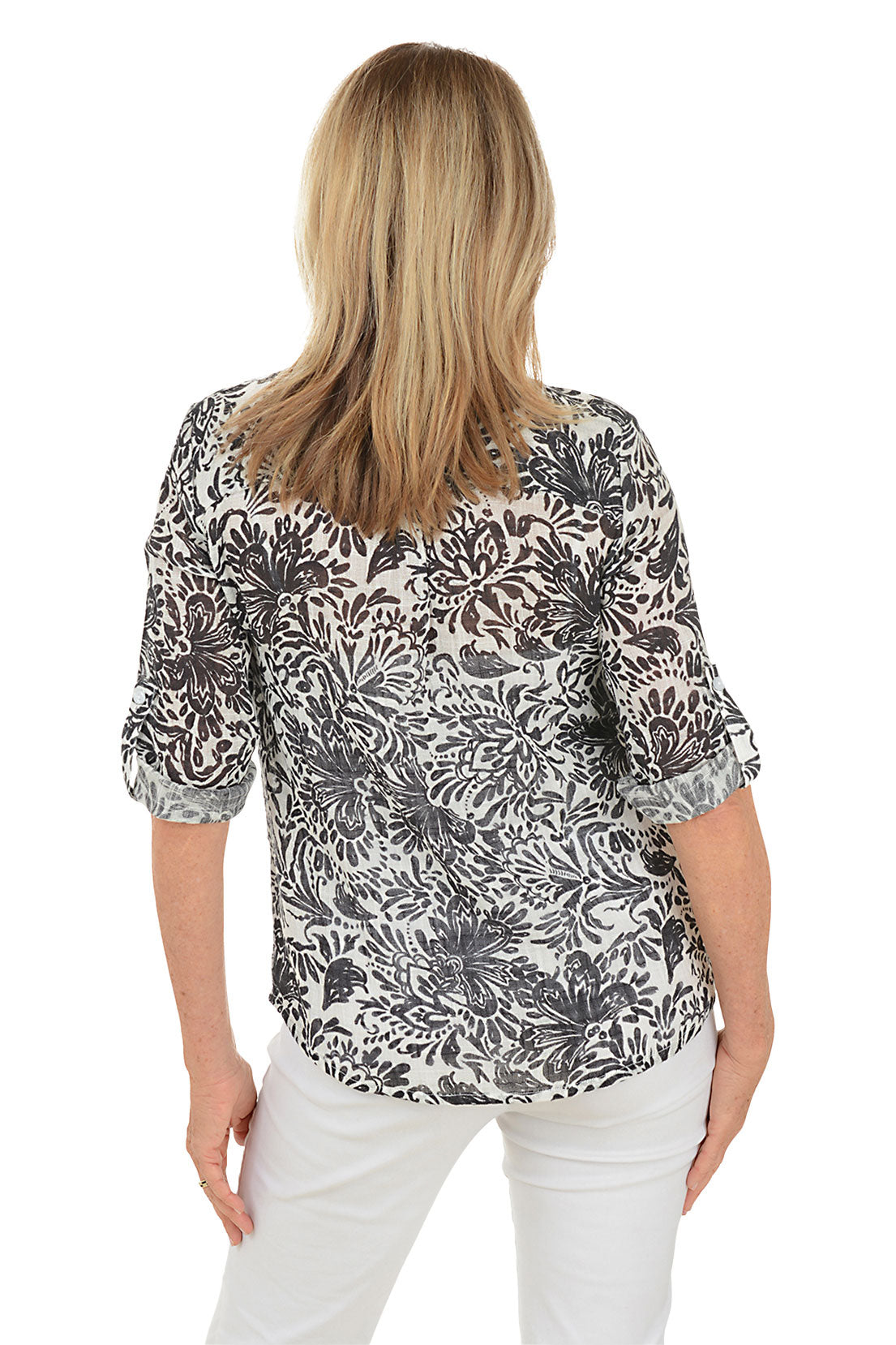 A woman wearing a floral gauze fabric henley blouse with a mandarin collar and 3/4 sleeves with button roll tabs. Back shot.