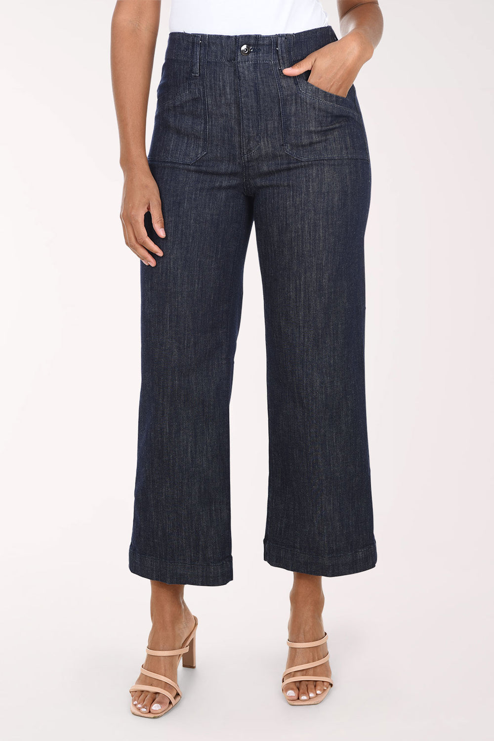 A model wearing dark wash cropped wide-leg denim jeans with a white top and beige heeled sandals, shown from the waist down against a plain white studio background.