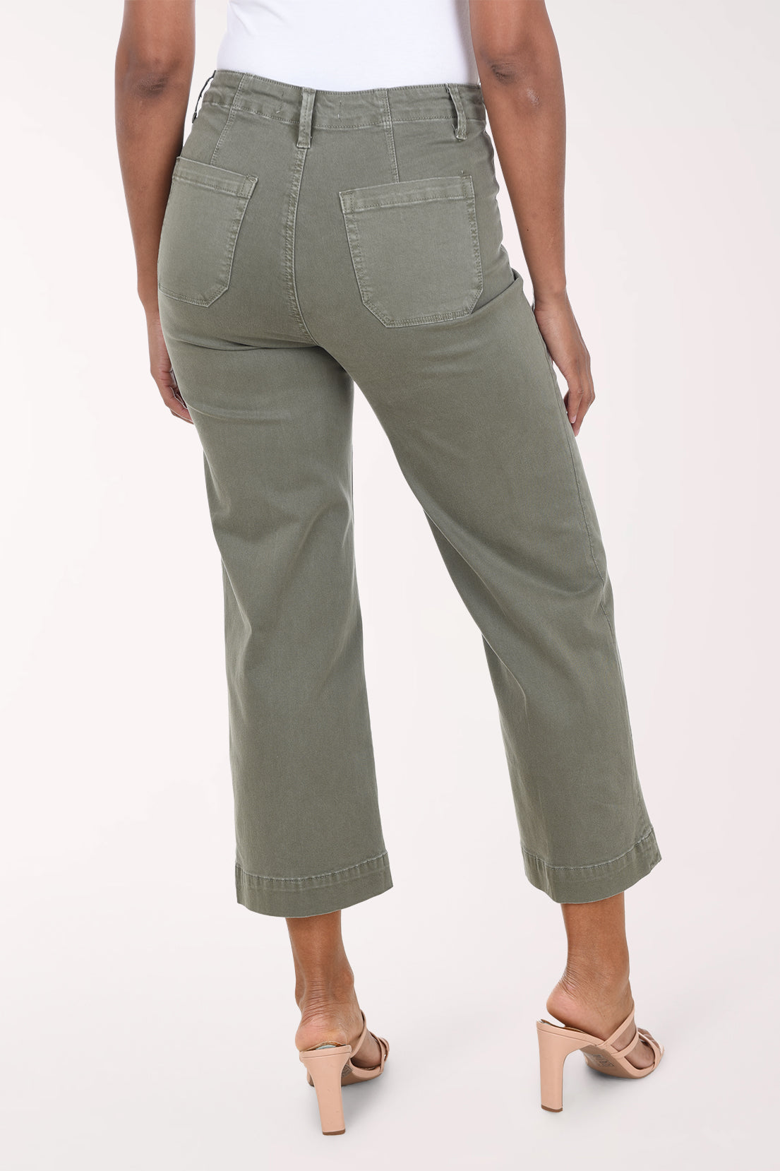 A model wearing olive green cropped wide-leg jeans with a white top and beige heeled sandals, shown from the waist down against a light studio background.
