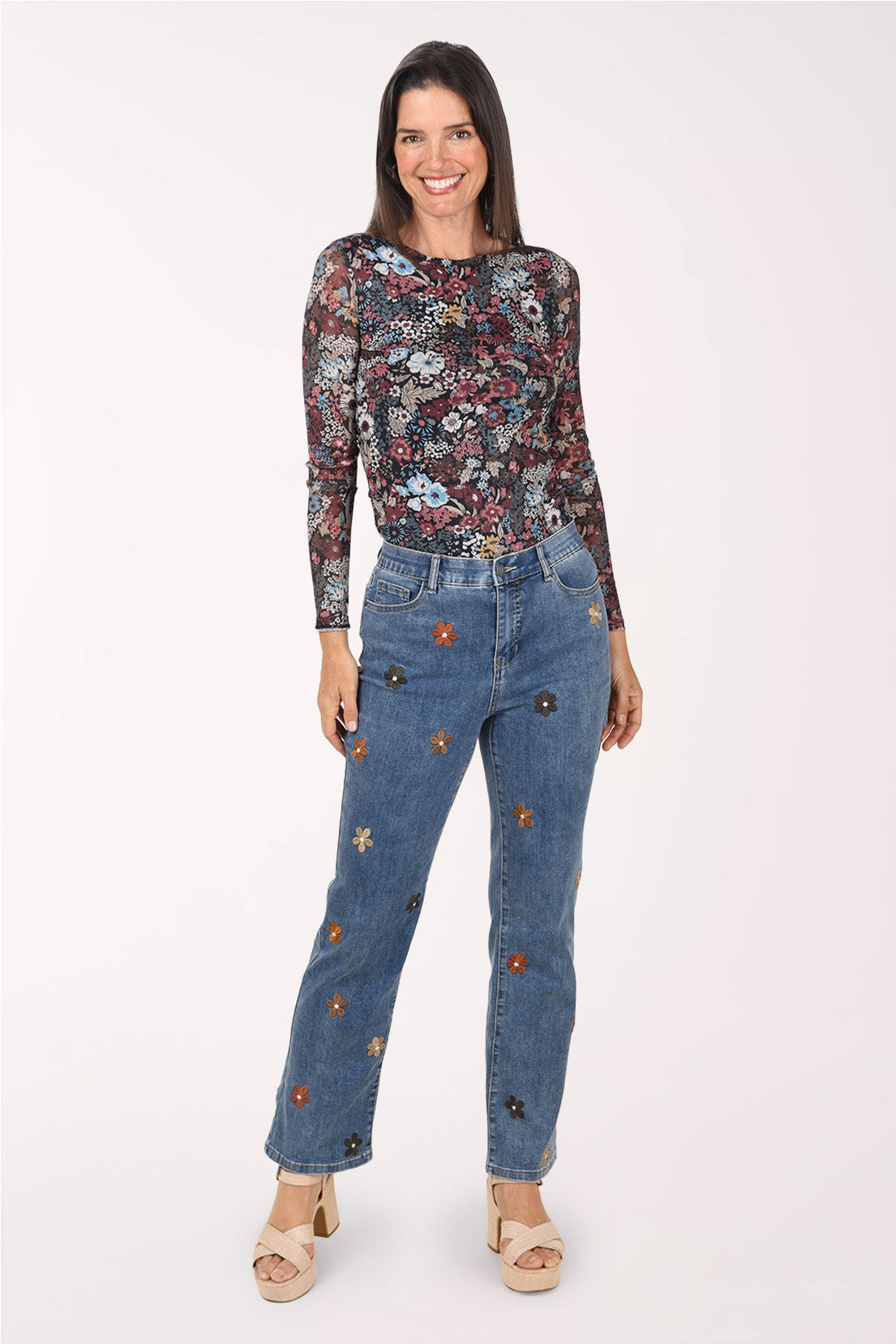 A full length front view of the embroidered flower jeans with a floral top and heeled sandals.