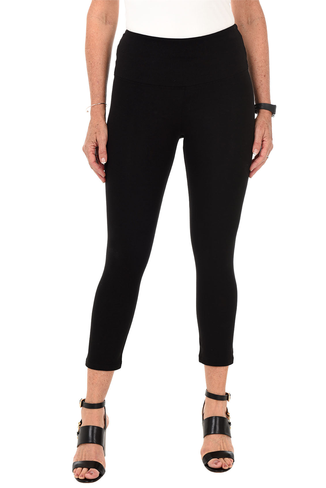 A front shot of a model wearing a pair of black pull-on cropped leggings with a wide elasticized waistband paired with black heels.