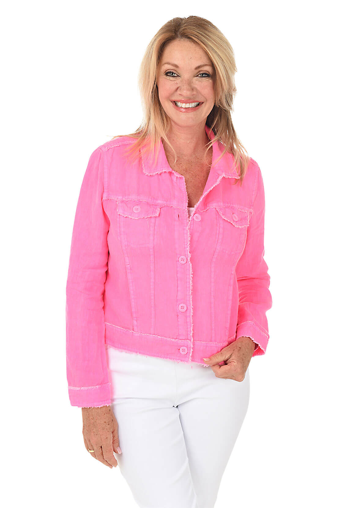 A smiling woman in a pink jacket and white pants stands against a white studio background.