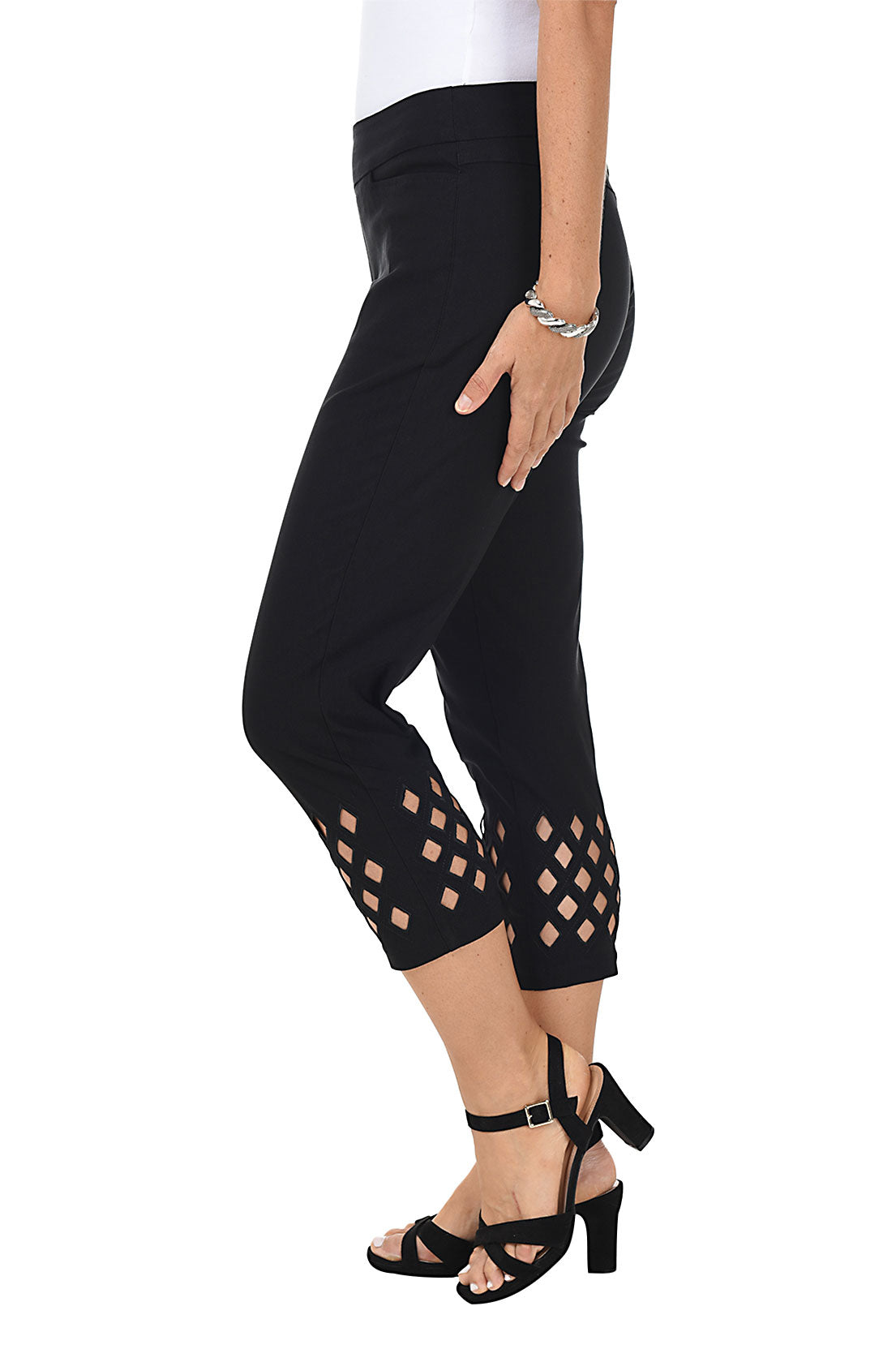 A woman wearing black cropped trousers with diamond eyelet cut-outs at the hem. Side shot.