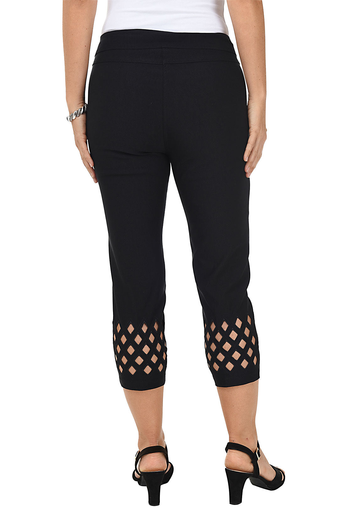 A woman wearing black cropped trousers with diamond eyelet cut-outs at the hem. Back shot.