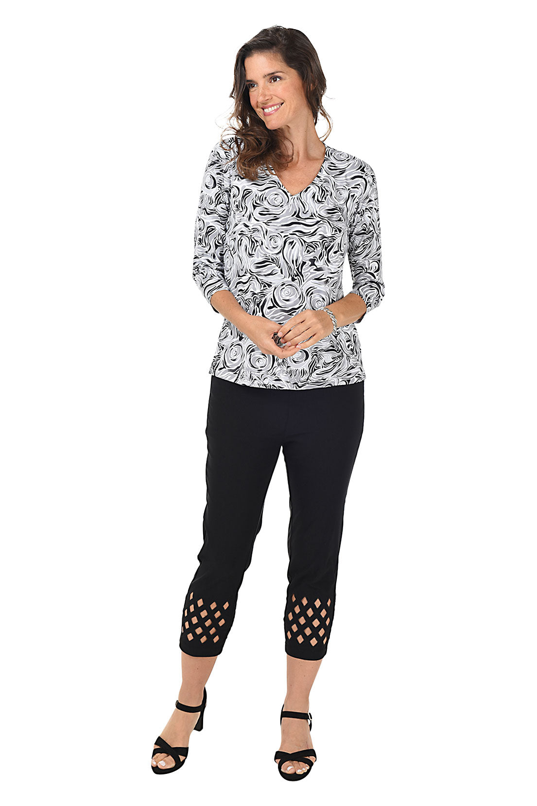 A woman wearing black cropped trousers with diamond eyelet cut-outs at the hem. Full length shot.