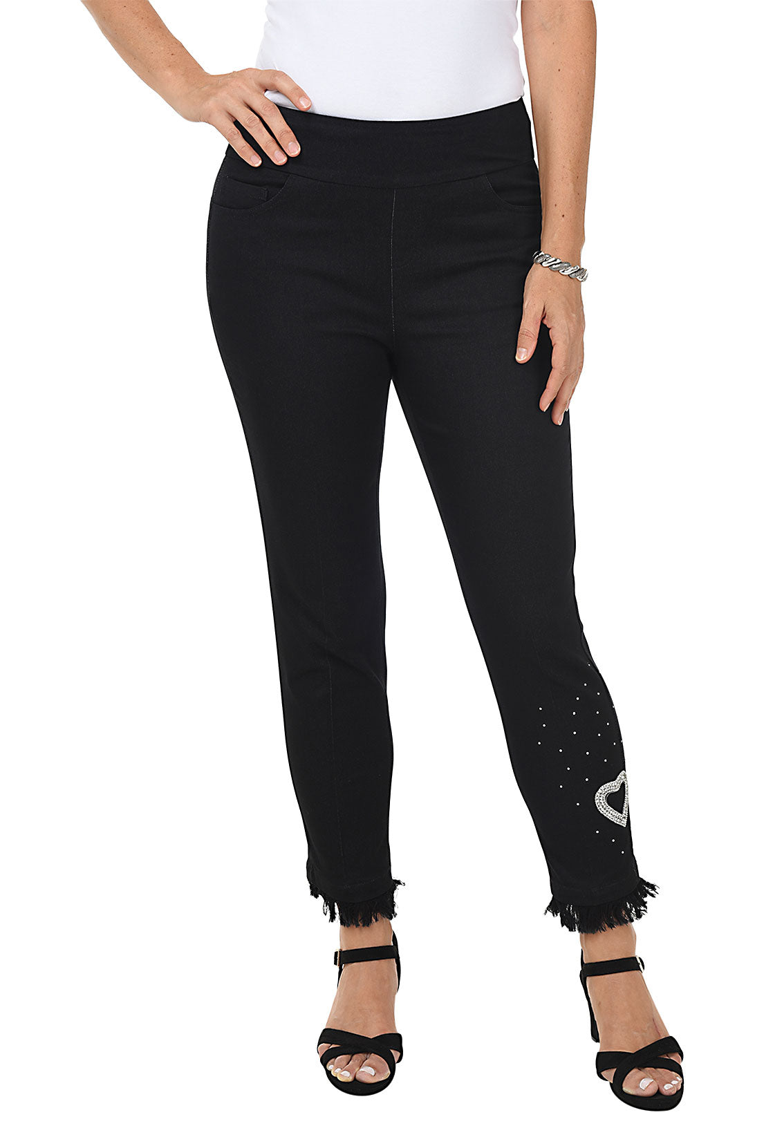 A woman wearing black denim ankle length jeans with a heart-shaped rhinestone applique and frayed hemline.