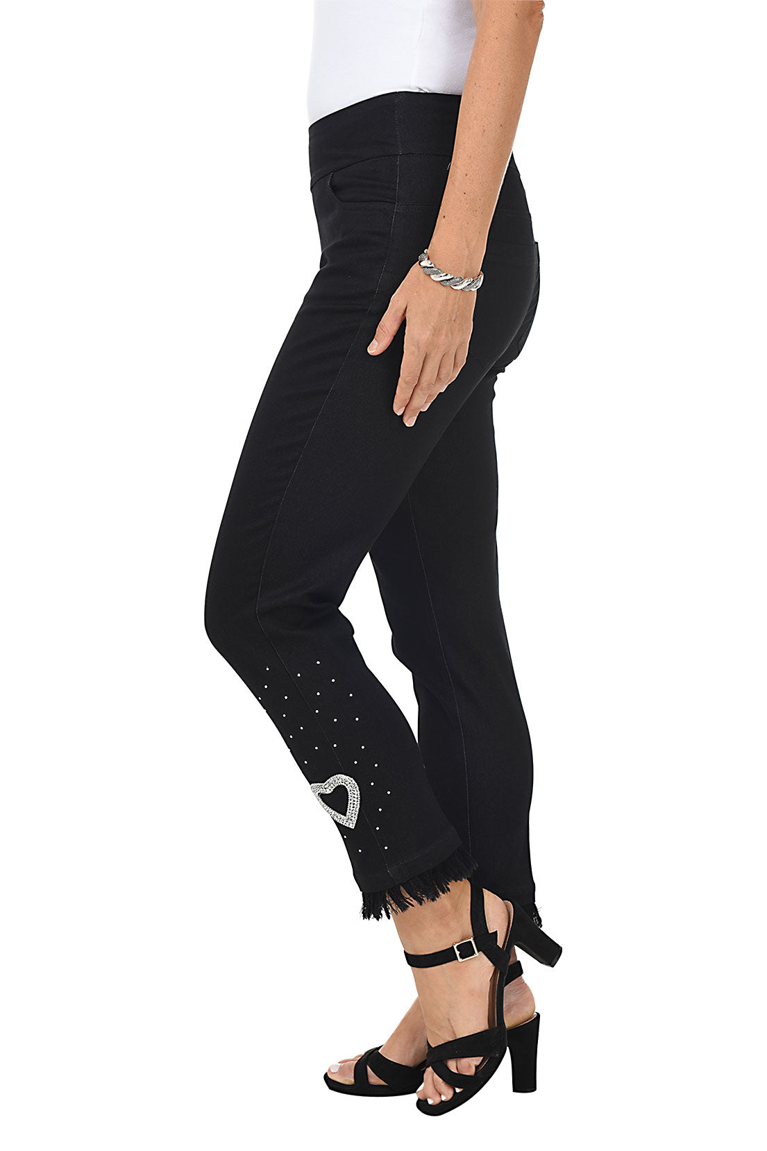 A woman wearing black denim ankle length jeans with a heart-shaped rhinestone applique and frayed hemline. Side shot.