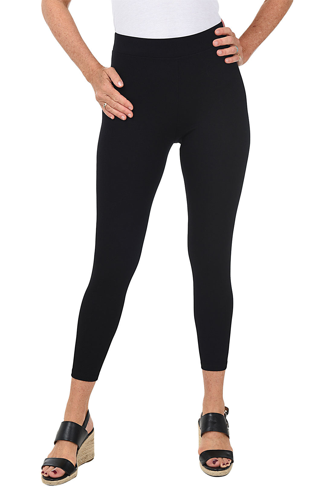 A woman wearing black ankle length leggings with a rhinestone-accented zipper on the back hemline.