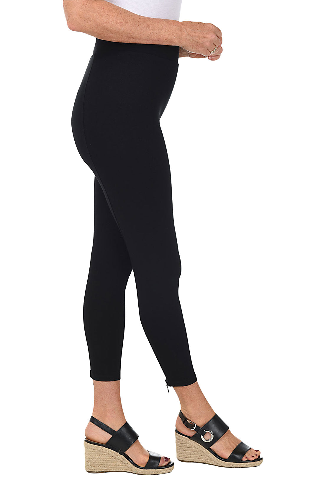 A woman wearing black ankle length leggings with a rhinestone-accented zipper on the back hemline. Side shot.