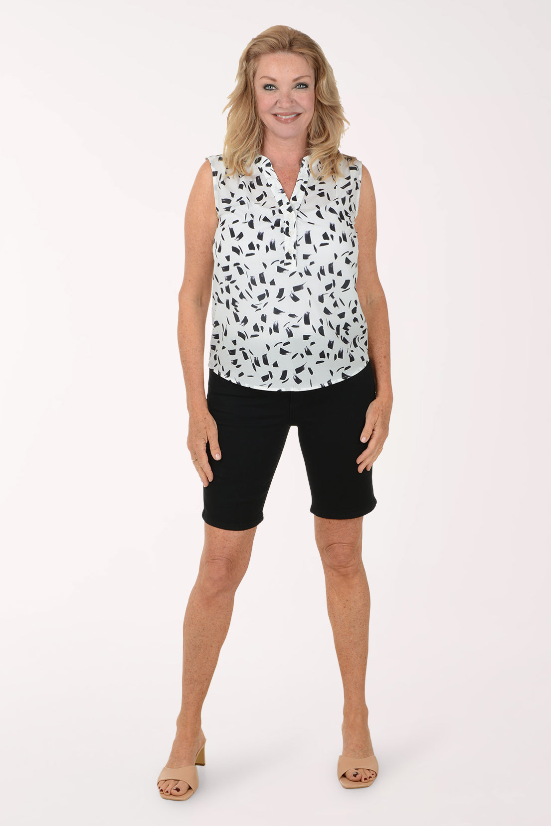 Woman wearing a sleeveless patterned top and black shorts on a white background