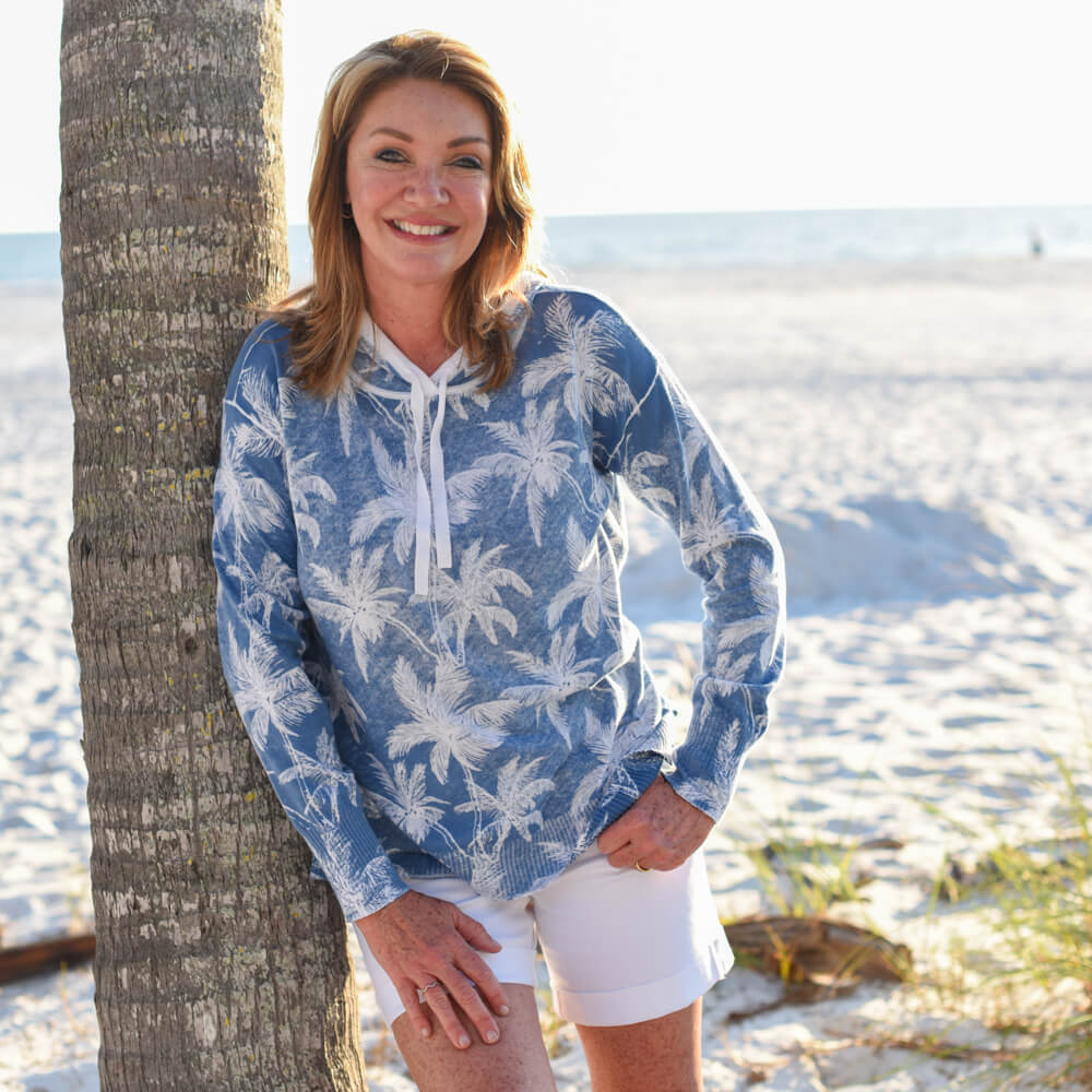 Woman wearing a blue palm tree patterned hoodie on a beach.