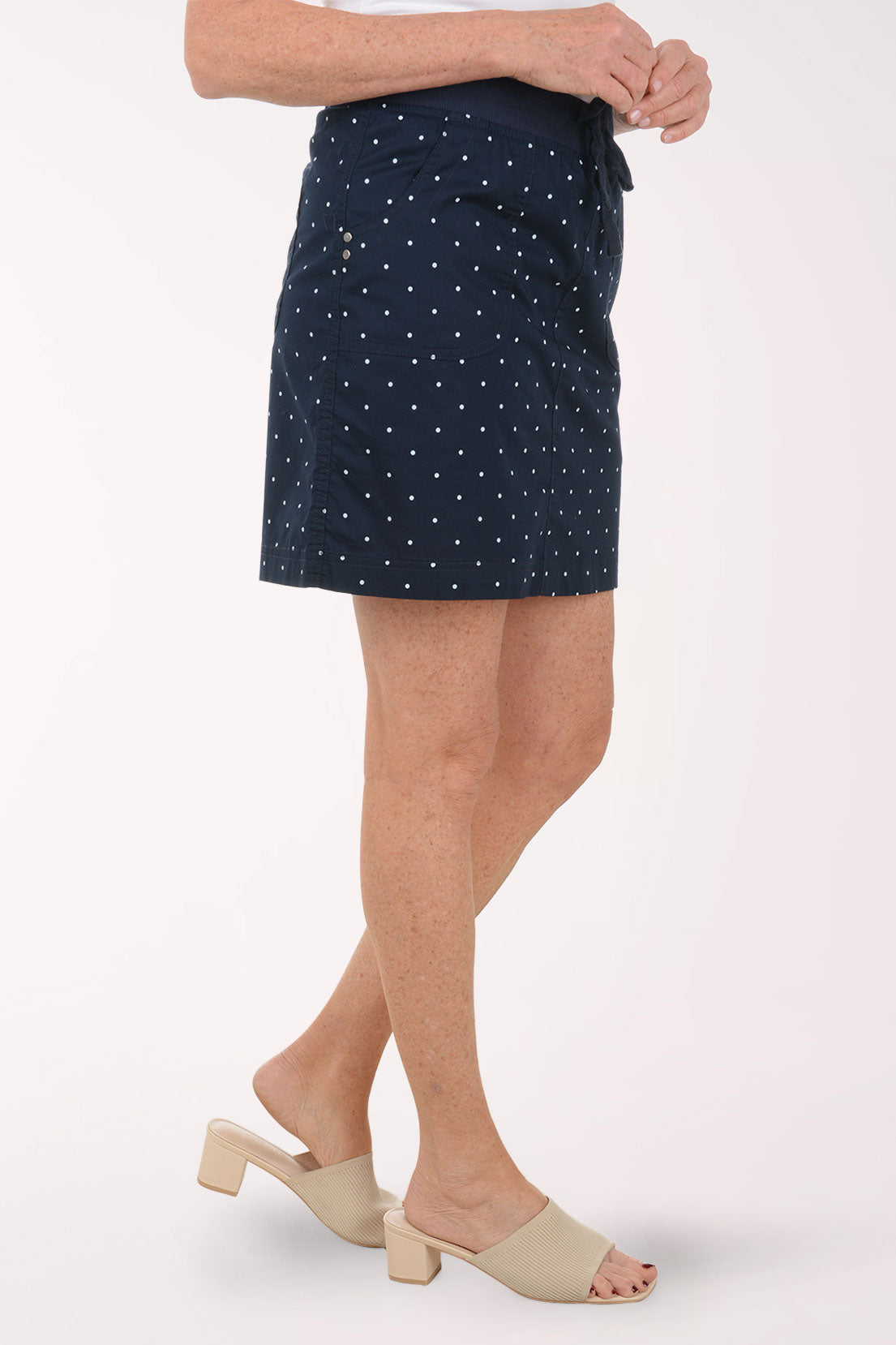 Person wearing a navy skirt with white polka dots on a white background
