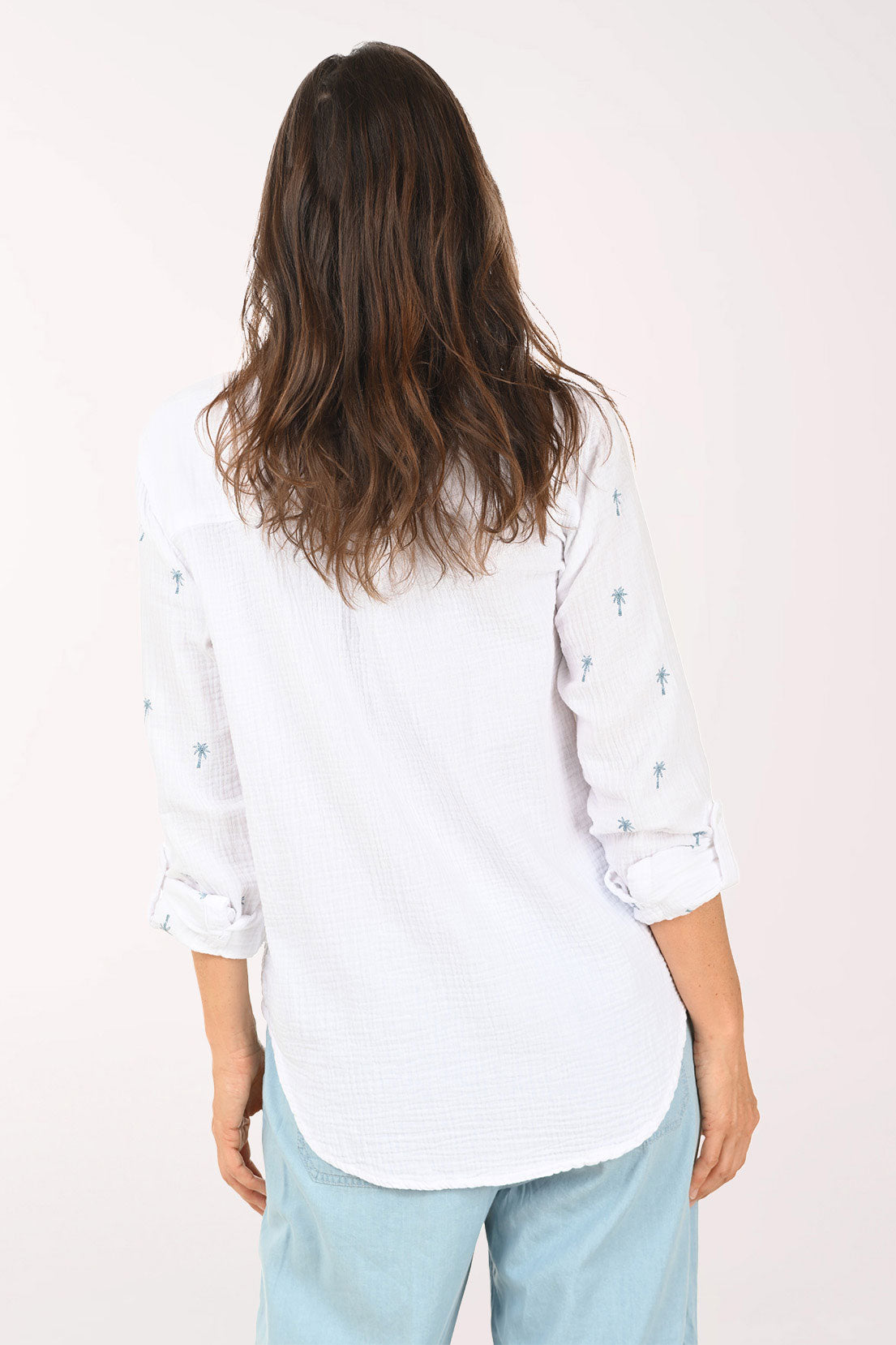 Woman wearing a 3/4 sleeve white top with embroidered palm trees