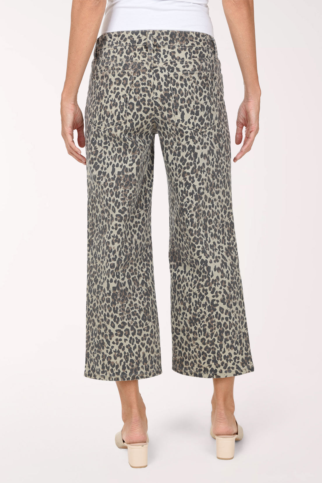 A person wearing cropped wide-leg pants with an olive green, black, and beige animal print, paired with a white top and beige slide sandals, against a plain white studio background.
